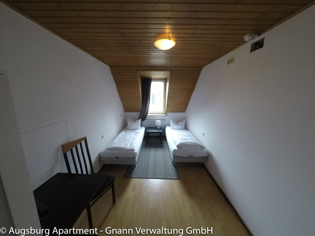 Zweibettzimmer mit Holzdecke und Tisch – Monteurzimmer Augsburg IV